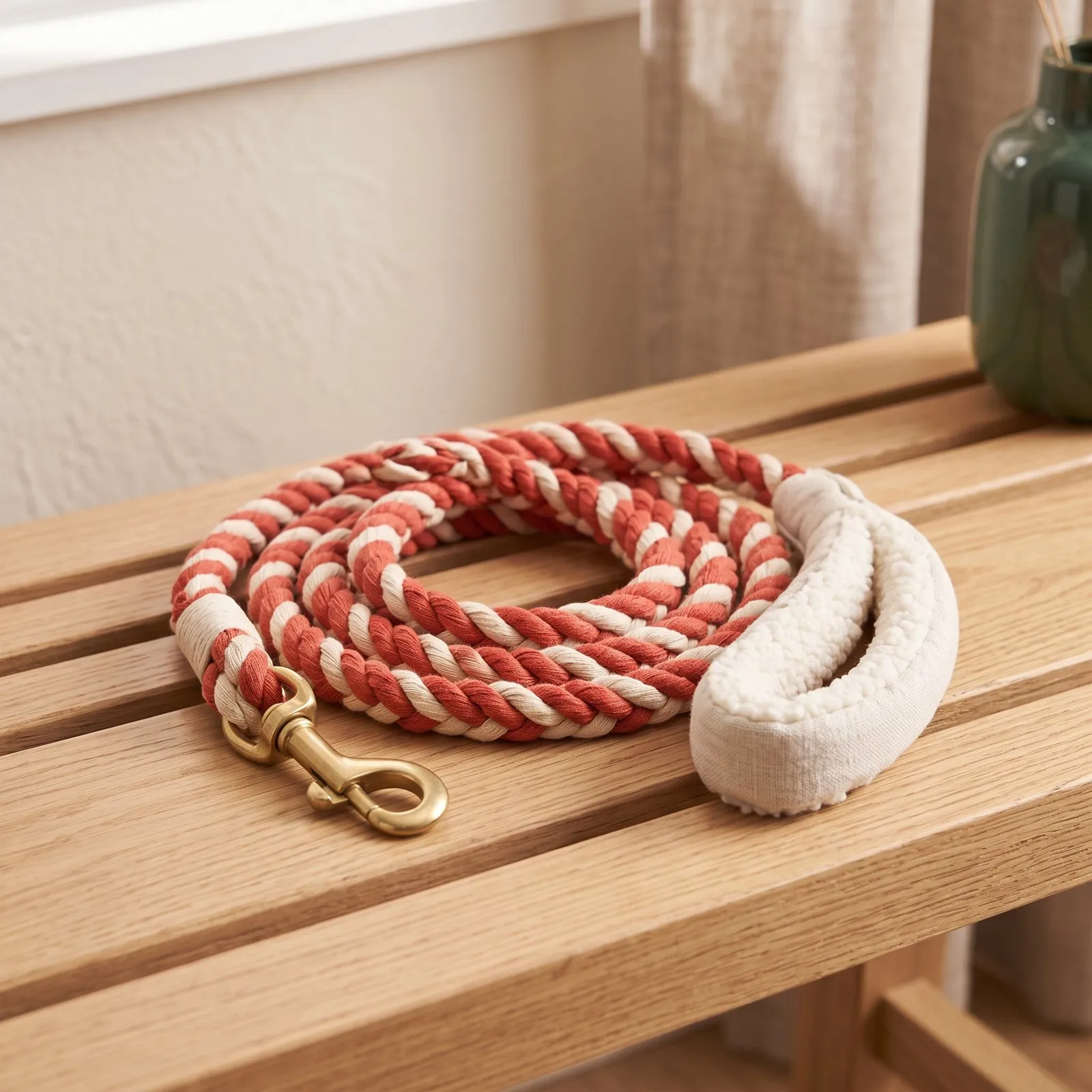 Red and cream braided rope leash coiled on a wooden bench, with a padded handle and a brass clip